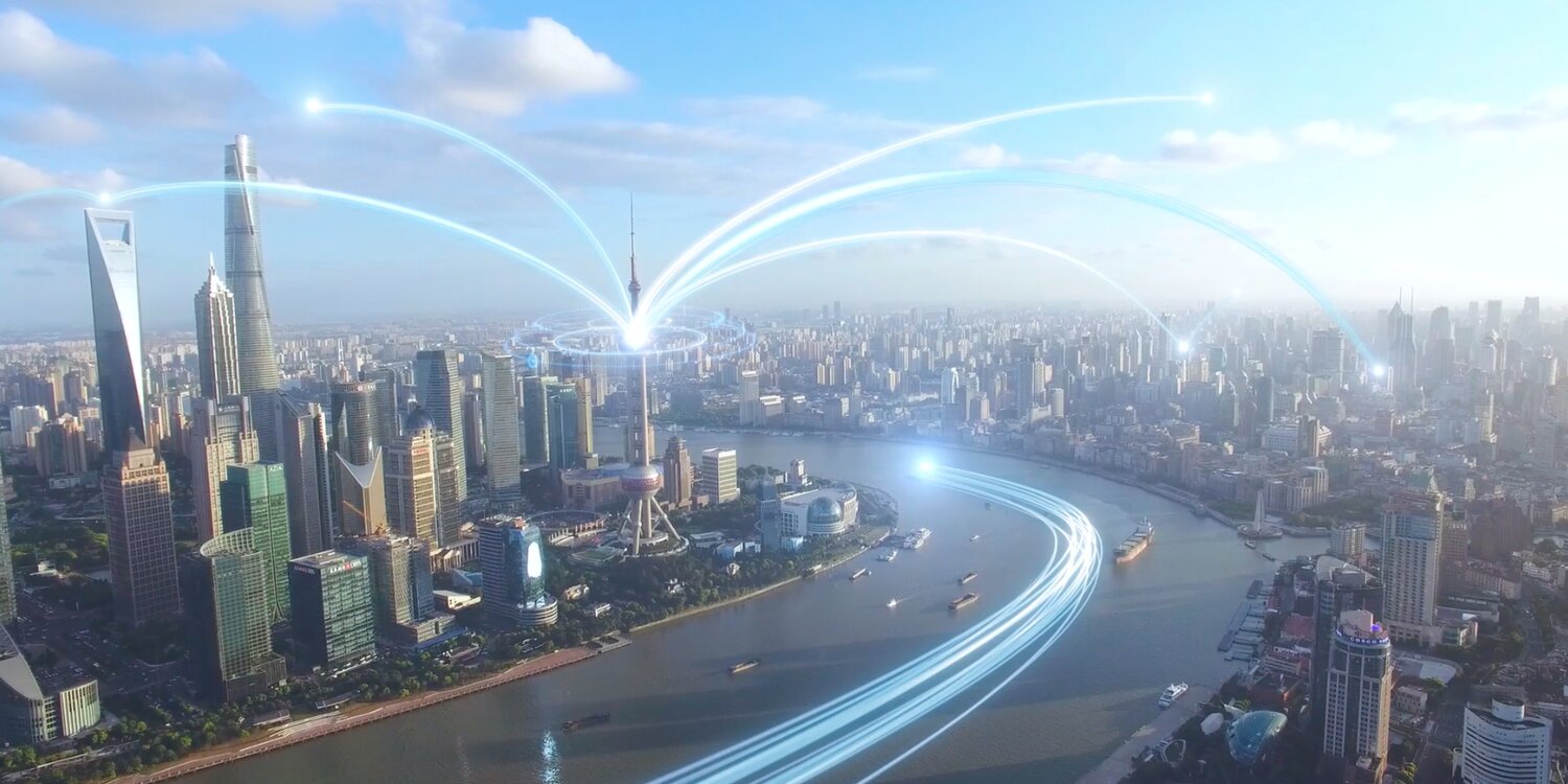 Videostill mit Blick von oben auf eine moderne Großstadt mit Flusskrümmung, wobei von einem Fernsehturm aus und über den Fluss Datenströme laufen