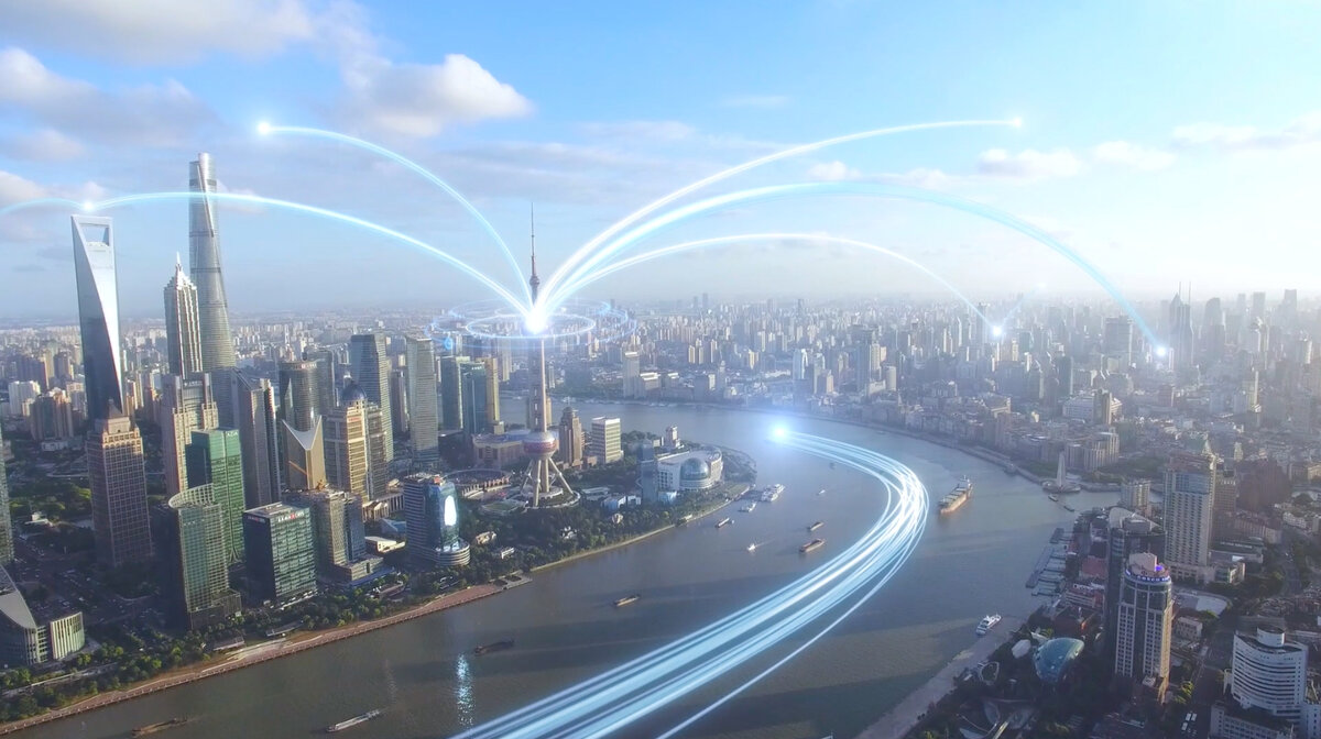 Videostill mit Blick von oben auf eine moderne Großstadt mit Flusskrümmung, wobei von einem Fernsehturm aus und über den Fluss Datenströme laufen